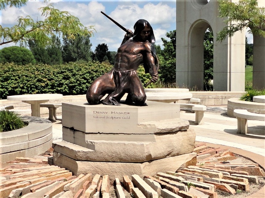 A bronze statue of a person with a sword, set in a park-like environment.
