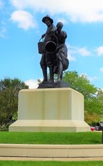 A bronze statue of two figures, one holding a drum, on a pedestal under a clear sky.